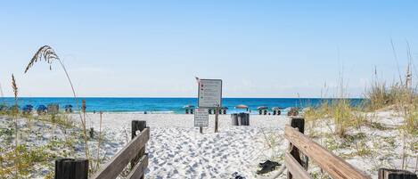 A wooden boardwalk leading to a beach with a signboard and trash bins.