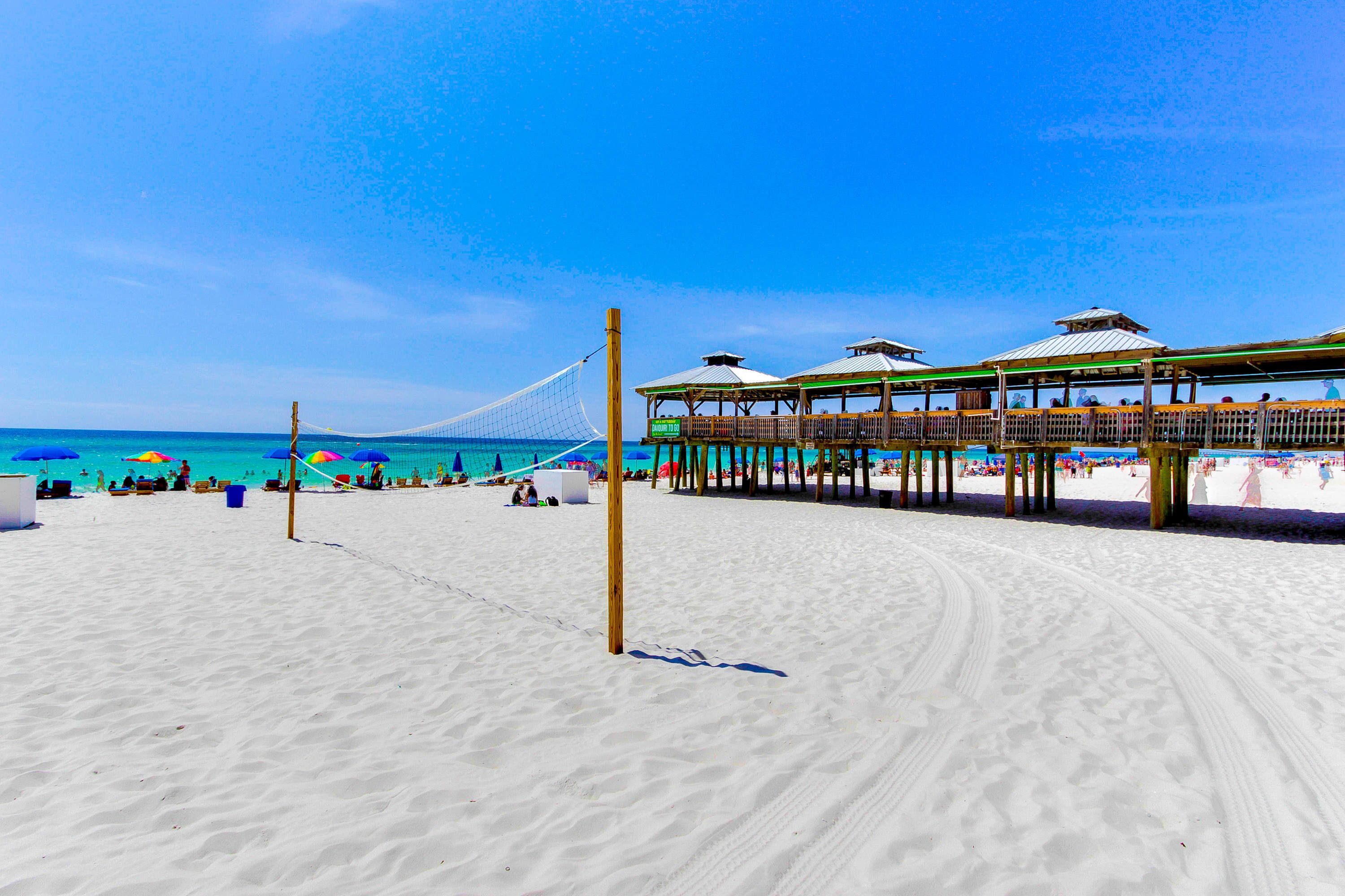 Une plage avec un filet de volley-ball, des parasols et une structure en bois dotée d’un toit.