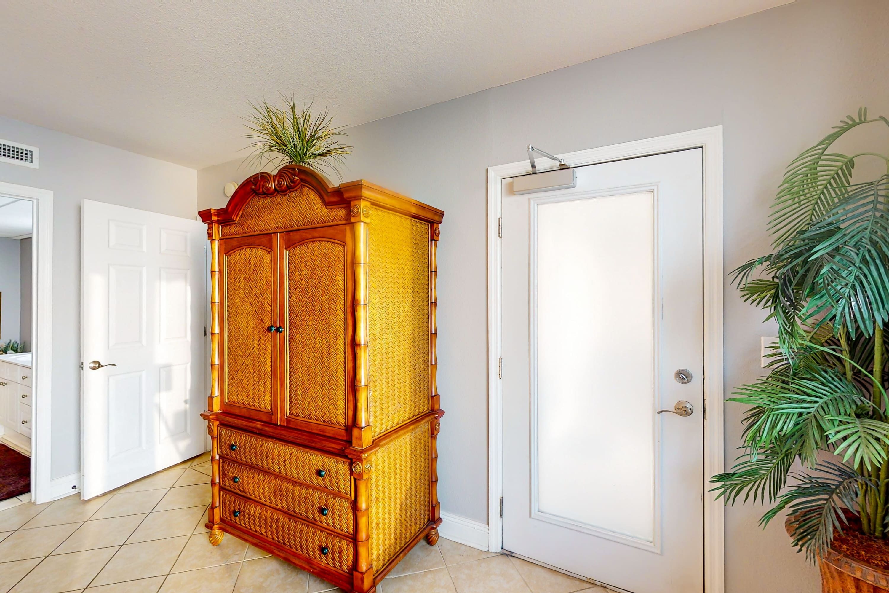A hallway with a wooden armoire, a white door, and a potted plant.