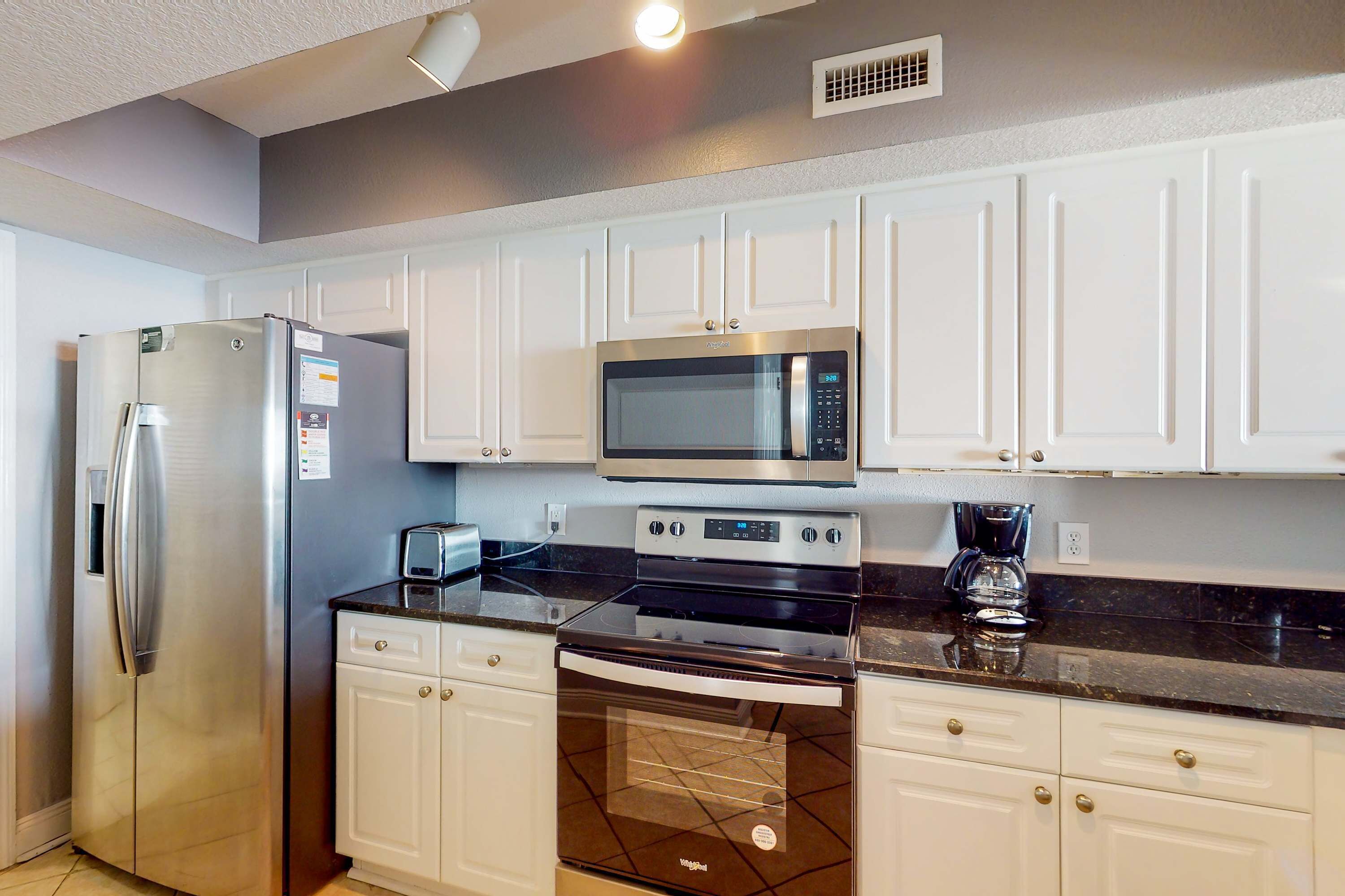 A modern kitchen with white cabinets, stainless steel appliances including a refrigerator, microwave, stove, and dishwasher.