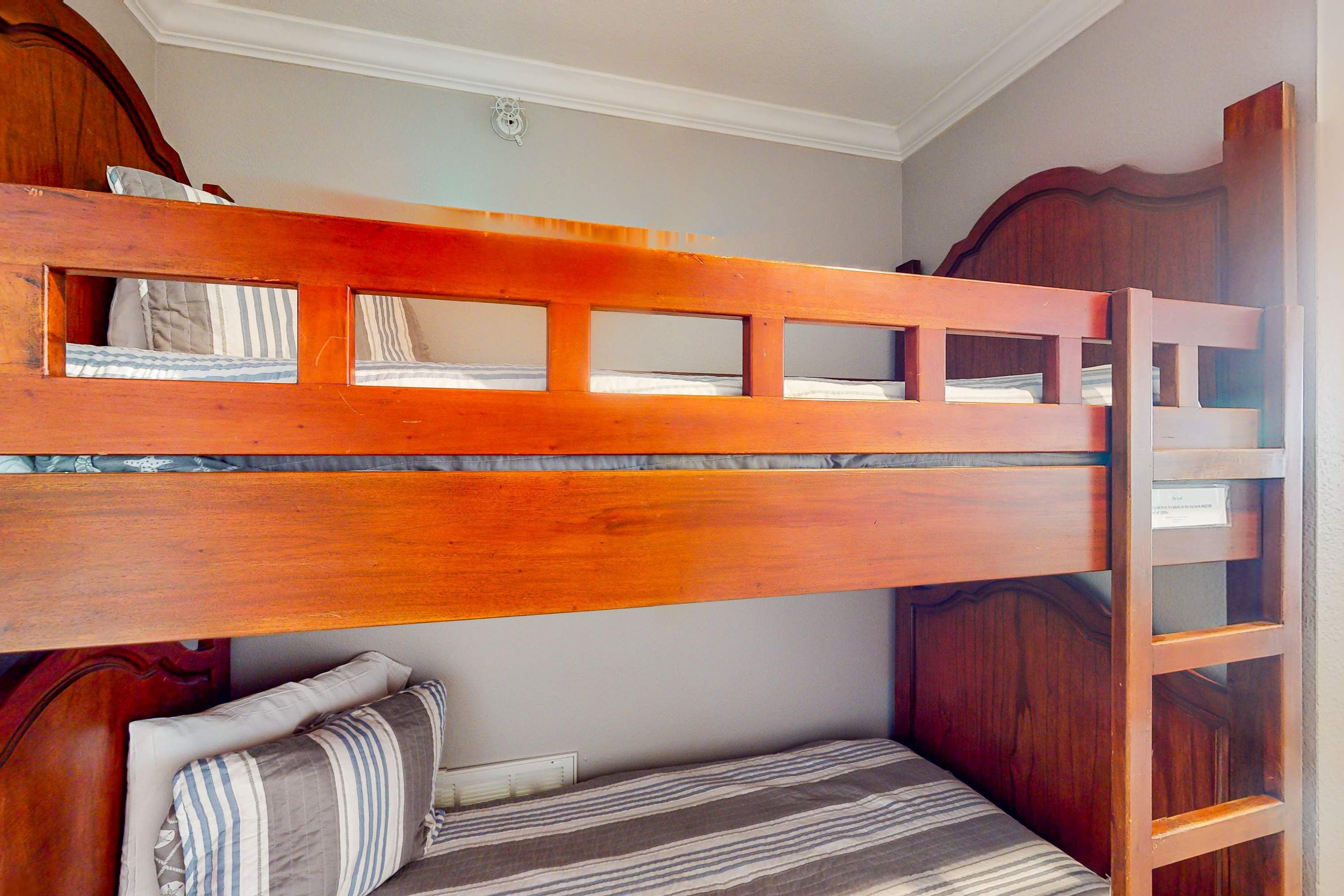 Una cama individual sobre otra, con estructura de madera, una escalera y un colchón a rayas.