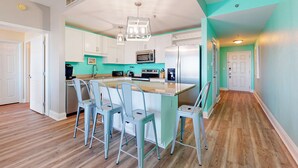 A modern kitchen with white cabinets, a central island with bar stools, a stainless steel refrigerator, and a microwave. - Water View Condo with Balcony, Central AC, WiFi, Pool/Hot Tub/Gym - Snowbirds OK (Panama City Beach)