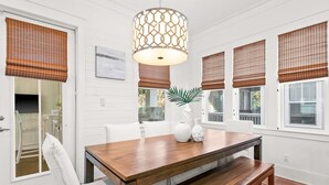 A dining area with a wooden table, white chairs, and a hanging light fixture. - Modern beachside haven with LSV and gas grill - bike to Blue Mt Beach (Santa Rosa Beach)