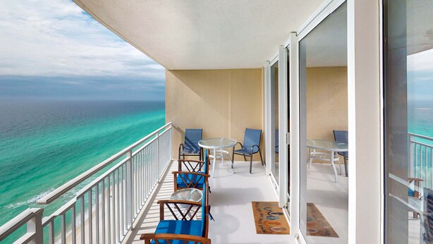 Un balcone con vista sull'oceano, arredato con sedie e un tavolo.