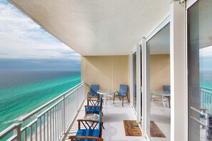 A balcony with a view of the ocean, furnished with chairs and a table. - Beautiful condo with beach access, shared pool, WiFi, and panoramic views (Panama City Beach)