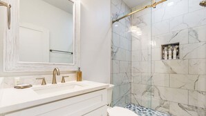 A bathroom with a white sink, gold faucets, a large mirror, and a shower with marble tiles. - Beautiful dog-friendly condo, private washer&dryer and close to beach (Navarre)