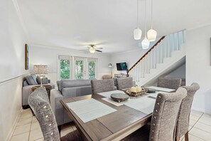 A dining area with a wooden table, grey upholstered chairs, and hanging pendant lights. - Lakefront Duplex with High-Speed Wi-Fi, Short Walk to Beach, and Water View (Santa Rosa Beach)