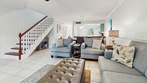 A modern living room with a staircase, grey sofas, a leather ottoman, and a ceiling fan. - Lakefront Duplex with High-Speed Wi-Fi, Short Walk to Beach, and Water View (Santa Rosa Beach)