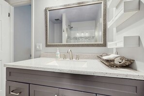 A bathroom with a white sink, a large mirror with a decorative frame, and a wicker basket on the counter. - Lakefront Duplex with High-Speed Wi-Fi, Short Walk to Beach, and Water View (Santa Rosa Beach)