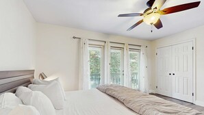 A bedroom with a bed, white curtains, a ceiling fan, and a view of greenery outside. - Lakefront Duplex with High-Speed Wi-Fi, Short Walk to Beach, and Water View (Santa Rosa Beach)
