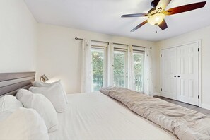 A bedroom with a bed, white curtains, a ceiling fan, and a view of greenery outside. - Lakefront Duplex with High-Speed Wi-Fi, Short Walk to Beach, and Water View (Santa Rosa Beach)