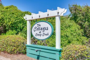Un letrero para "The Cottages at Camp Creek" con una estructura de pérgola blanca y una base verde.