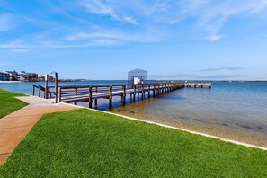 A pier extending into calm waters with a grassy area and benches along the walkway. - Cozy coastal condo with water view, pool, central AC, & easy beach access (Navarre Beach)