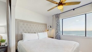 Una camera da letto con un letto grande, un ventilatore a soffitto, un comodino e una finestra vista mare.