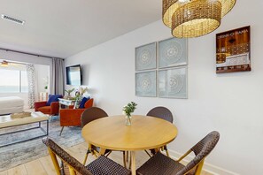 A modern living room with a round wooden table, wicker chairs, a TV, and decorative wall art. - Cozy coastal condo with water view, pool, central AC, & easy beach access (Navarre Beach)