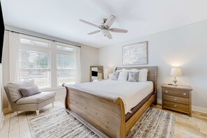 A bedroom with a wooden bed, a nightstand with a lamp, a chair, and a ceiling fan. - Charming home with enclosed sunroom, porch, central AC, & W&D - near beach (Santa Rosa Beach)