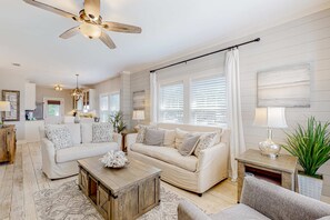 A spacious living room with a beige sofa, a wooden coffee table, and a ceiling fan. - Charming home with enclosed sunroom, porch, central AC, & W&D - near beach (Santa Rosa Beach)