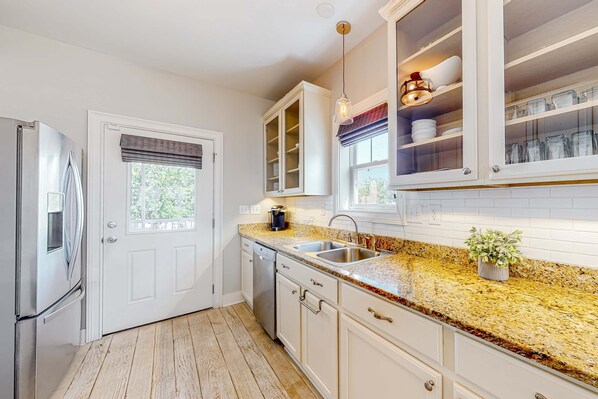A kitchen with white cabinets, a granite countertop, a stainless steel refrigerator, and a dishwasher. - Charming home with enclosed sunroom, porch, central AC, & W&D - near beach (Santa Rosa Beach)