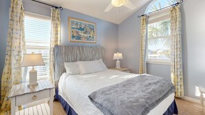 Ein Schlafzimmer mit einem Bett, zwei Nachttischen mit Lampen, einem Deckenventilator und Vorhängen.