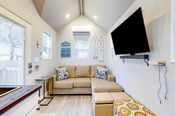 A modern living room with a beige sectional sofa, a flat-screen TV mounted on the wall, and a small side table.