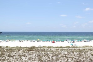 A beach with white sand, clear blue water, and several colorful umbrellas. - Updated 3rd floor condo w/ beach access and complementary BEACH SERVICE (Navarre Beach)