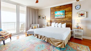 Een hotelkamer met een groot bed, een plafondventilator, een houten accentmuur, een klok en uitzicht op het buitengebied.