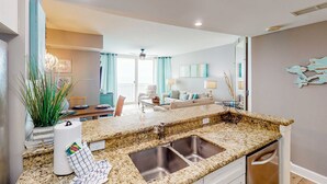 A modern kitchen with granite countertops, a double sink, and a dining area with a table and chairs. - 16th-floor condo with Gulf views, beach access, 2 pools, hot tub, & private W&D (Panama City Beach)