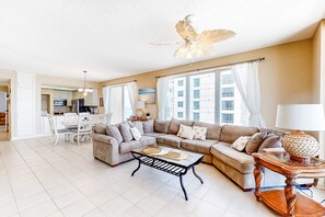 A spacious living room with a sectional sofa, a coffee table, and a dining area with a white table and chairs. - 11th Floor Gulf Front Condo Great Amenities & Private Beach Access (Navarre Beach)