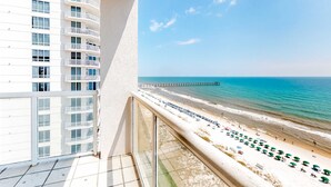 Un balcone con vista su una spiaggia, un molo e un grattacielo.