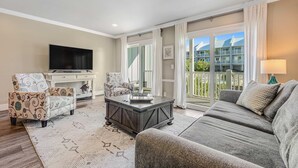 Un salon comprenant un canapé, deux fauteuils, une table basse, un téléviseur à écran plat et un balcon offrant une vue sur les immebles.