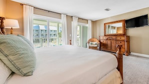 Une chambre avec un grand lit, une commode, une télévision et un balcon avec des rideaux.