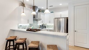 Una cocina moderna con armarios blancos, un refrigerador de acero inoxidable y una barra con taburetes.