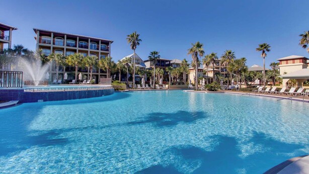 Una gran piscina con fuente, rodeada de palmeras y edificios de hotel.
