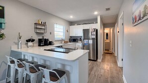 A modern kitchen with white bar stools, a stainless steel refrigerator, and a microwave. - Gorgeous home with private pool, outdoor space and close to beach (Panama City Beach)