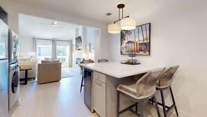 A modern kitchen with a central island, bar stools, and a dining area with a sofa. - Courtyard view condo with private beach access, private balcony, & free WiFi (Santa Rosa Beach)