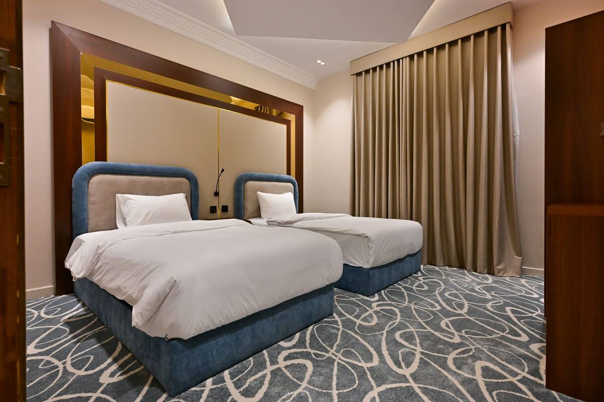 Una habitación de hotel con dos camas, alfombra estampada, un espejo grande y una ventana con cortinas.