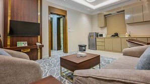 Une chambre d’hôtel équipée d’un canapé, d’une table basse, d’un téléviseur à écran plat et d’un coin cuisine comprenant un réfrigérateur, un four à micro-ondes et une machine à café.