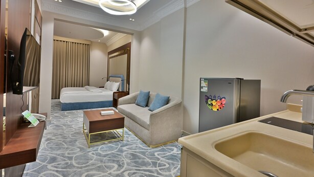 Une chambre d’hôtel comprenant un lit, un canapé, une petite table, un coin cuisine avec un évier et un réfrigérateur.