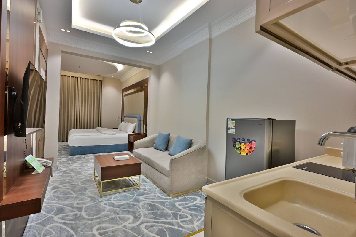 Habitación de hotel con cama, sofá, una mesita, espacio de cocina con pileta y refrigerador.