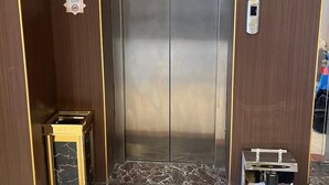 Un ascenseur avec une finition métallique, un lecteur de cartes d’accès numérique et une petite poubelle.