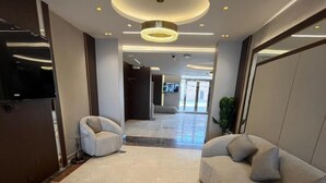 Un hall d’entrée moderne avec un sol en marbre, un canapé incurvé, un fauteuil et un grand lustre.