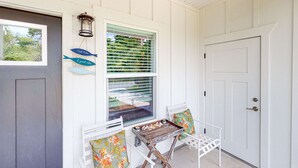 A porch with a white door, a window with blinds, a small table with a tray, and two white chairs with colorful cushions. - Newly built dog-friendly home with spacious backyard & private W&D (Panama City Beach)