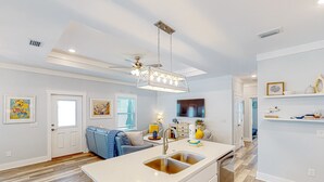 A modern kitchen with a central island, stainless steel sink, and a ceiling fan. - Newly built dog-friendly home with spacious backyard & private W&D (Panama City Beach)