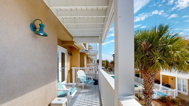 A balcony with white railings, a small table, and two chairs with patterned cushions. - Spacious house with patio, pool, balcony, deck, & W&D - beach access (Panama City Beach)