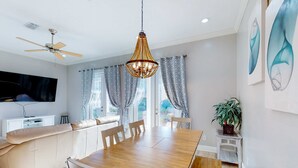 A modern living room with a wooden dining table, beige sofa, and a ceiling fan. - Spacious house with patio, pool, balcony, deck, & W&D - beach access (Panama City Beach)