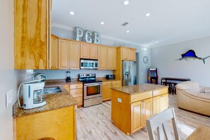 A modern kitchen with wooden cabinets, stainless steel appliances, and a granite countertop. - Spacious house with patio, pool, balcony, deck, & W&D - beach access (Panama City Beach)