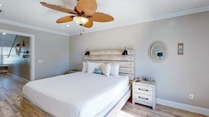 A bedroom with a large bed, wooden headboard, a ceiling fan, a bedside table, and a nightstand. - Spacious house with patio, pool, balcony, deck, & W&D - beach access (Panama City Beach)