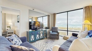 Habitació d'hotel moderna amb una finestra gran, televisió, sofà, cadira i taula petita.