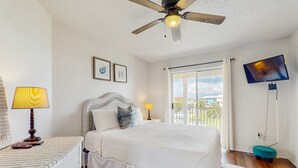 A bedroom with a bed, a ceiling fan, a TV, and a balcony with a view.