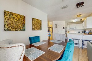 A dining area with a wooden table, blue chairs, and two large patterned wall hangings.